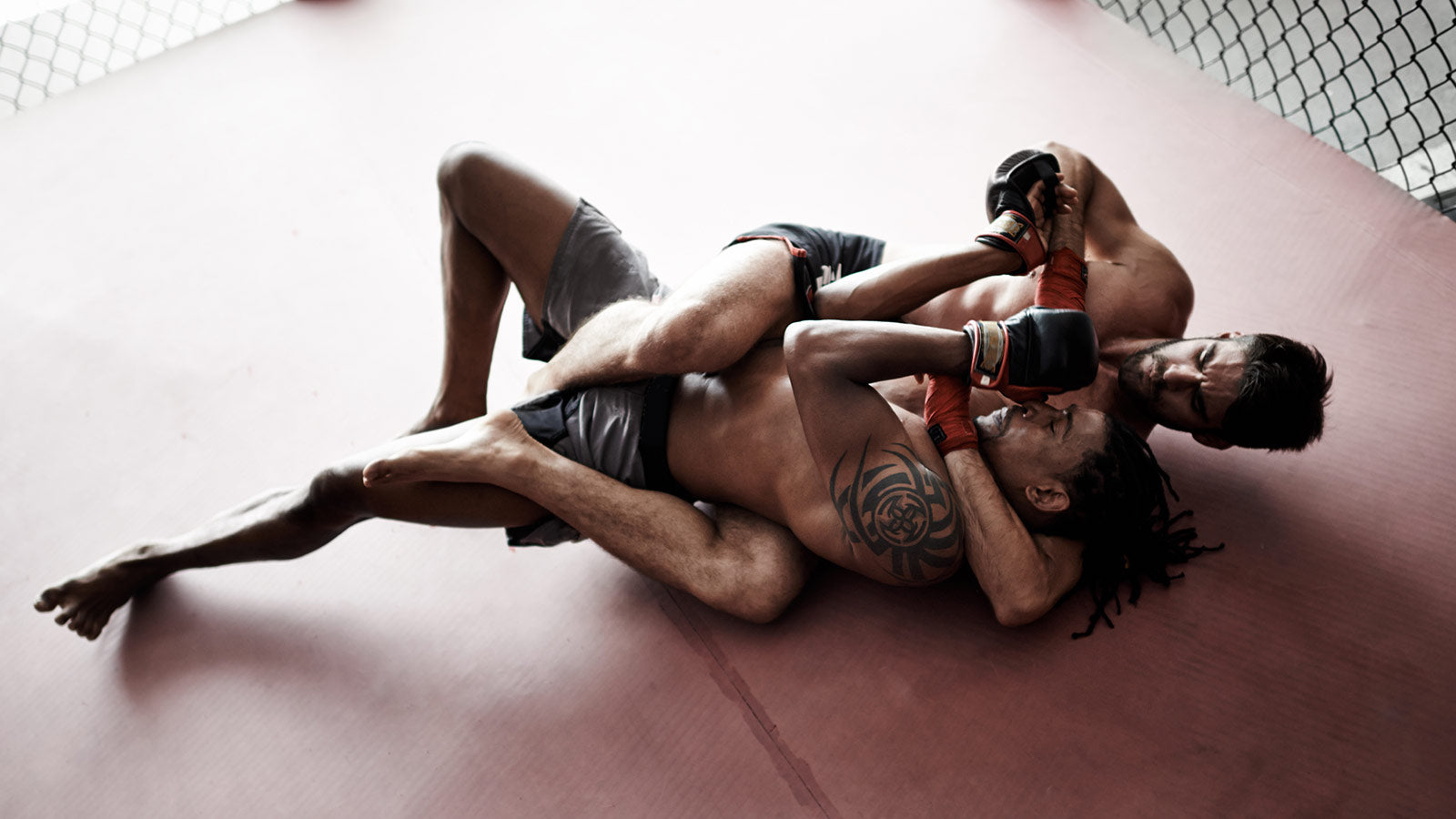 Two fighters in a cage fight position on a pink mat.