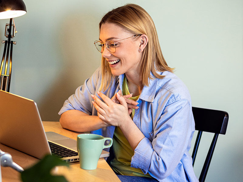 Woman sitting at a desk with a laptop, smiling and clapping hands.