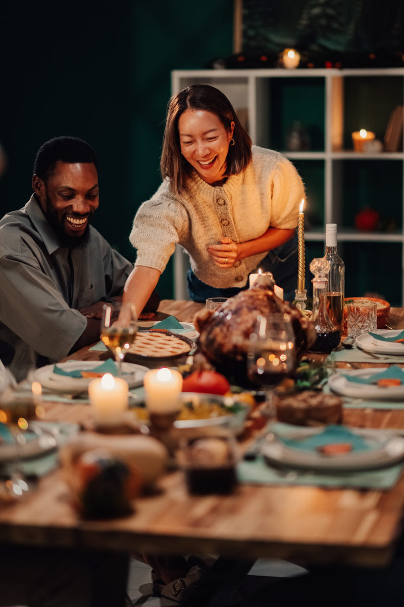 Two people sitting at a dinner table with candles and food, smiling and laughing.