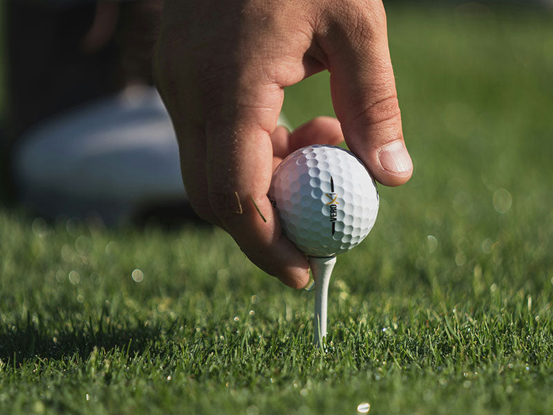 Hand placing a golf ball on a tee in a grassy field