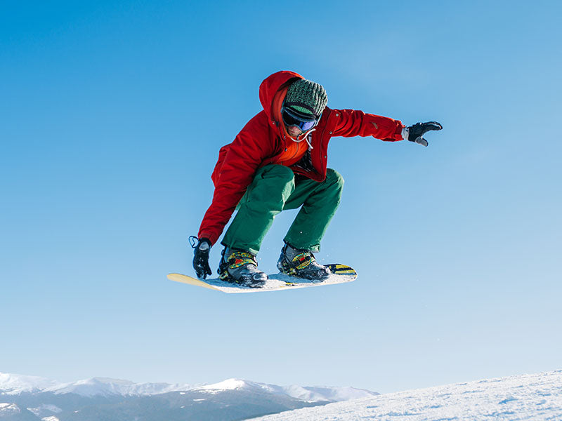 Person snowboarding in the air with a clear blue sky and mountains in the background